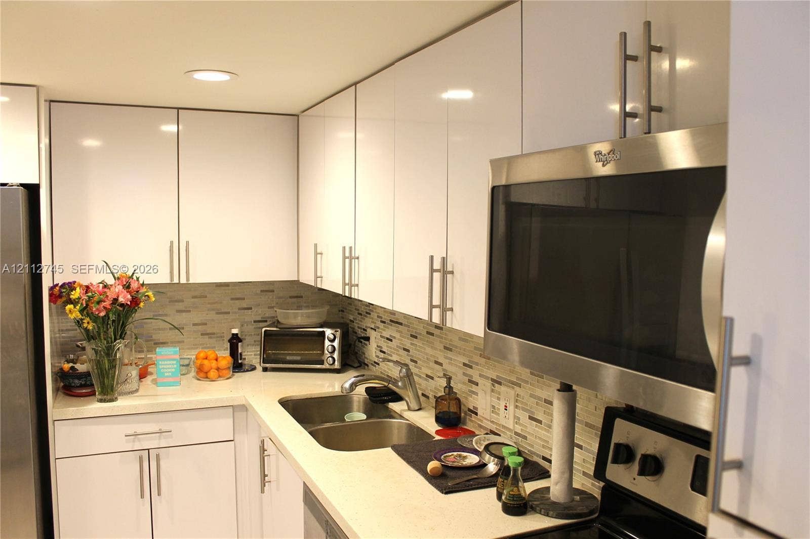 20500 W Country Club Drive, #202, Aventura, FL 33180 Glossy white cabinetry, solid-surface countertops, mosaic tile backsplash, recessed ceiling lighting, and stainless steel over-the-range microwave