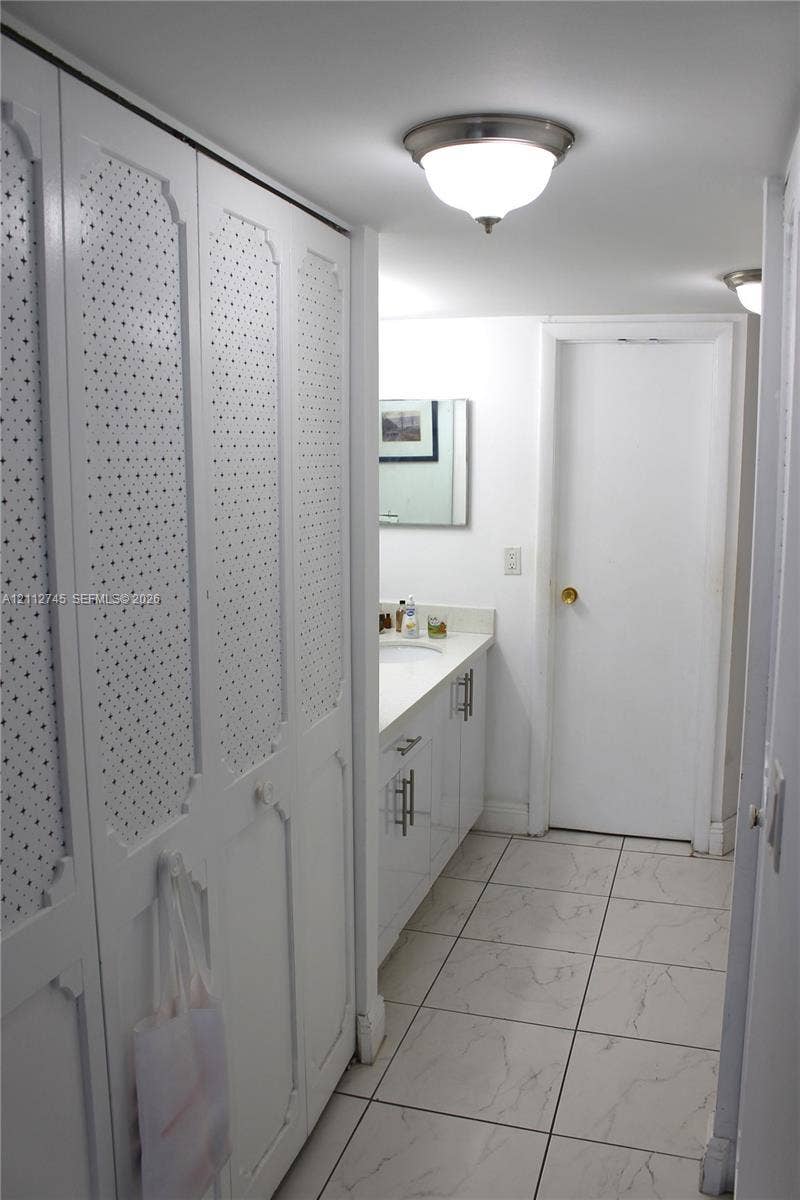 20500 W Country Club Drive, #202, Aventura, FL 33180 Floor-to-ceiling white cabinetry with textured detail, white vanity with rectangular under-mount sink, stone-finish tile flooring, and flush-mount lighting fixtures
