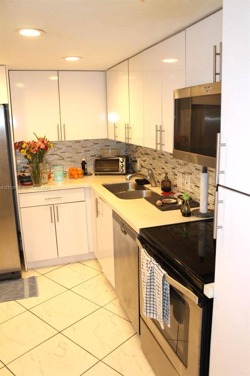 20500 W Country Club Drive, #202, Aventura, FL 33180 Kitchen featuring white high-gloss cabinetry, stainless steel appliances, tiled backsplash, solid surface countertops, and recessed lighting