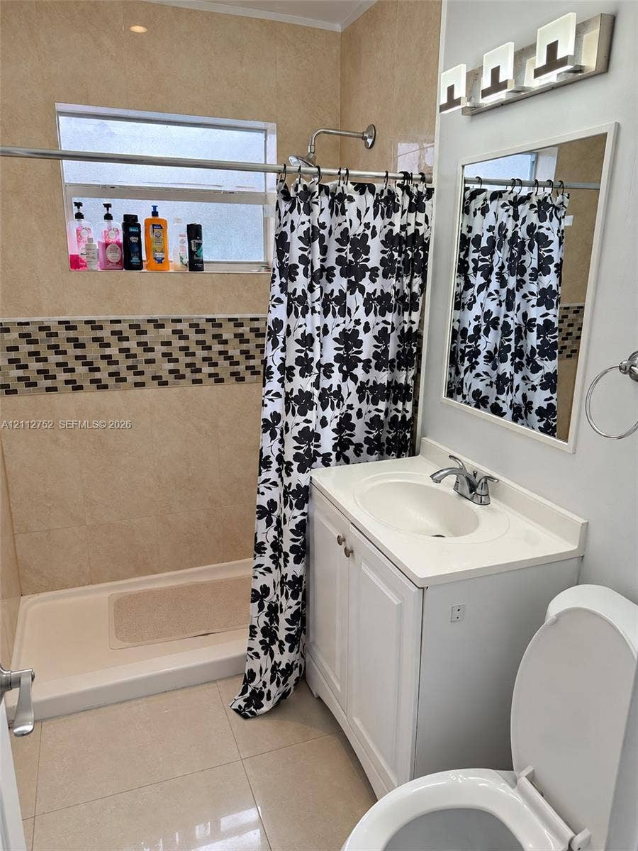 1210 N 71st Avenue, Hollywood, FL 33024 Full bathroom featuring tile wall finishes with mosaic accent inlay, a glass-enclosed shower, a white vanity with integrated basin, and modern multi-light fixture