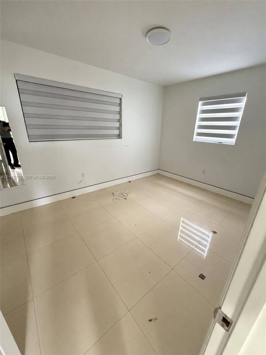 1210 N 71st Avenue, Hollywood, FL 33024 Neutral interior featuring large-format ceramic tile flooring, dual-layered roller shades, and a ceiling-mounted flush light fixture