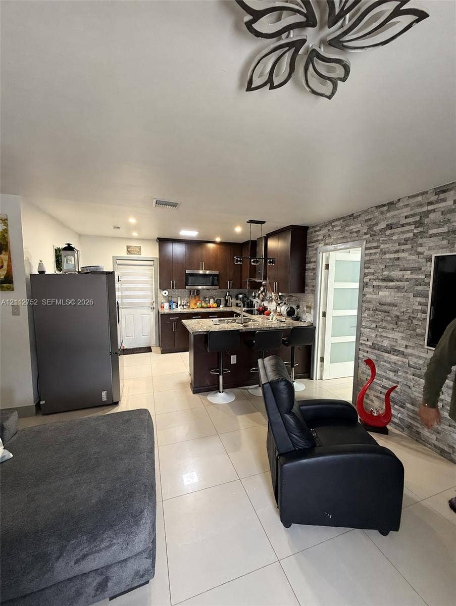 1210 N 71st Avenue, Hollywood, FL 33024 Kitchen featuring dark wood cabinetry, stone-finish countertops, stainless steel appliances, stacked-stone accent wall, and porcelain tile flooring