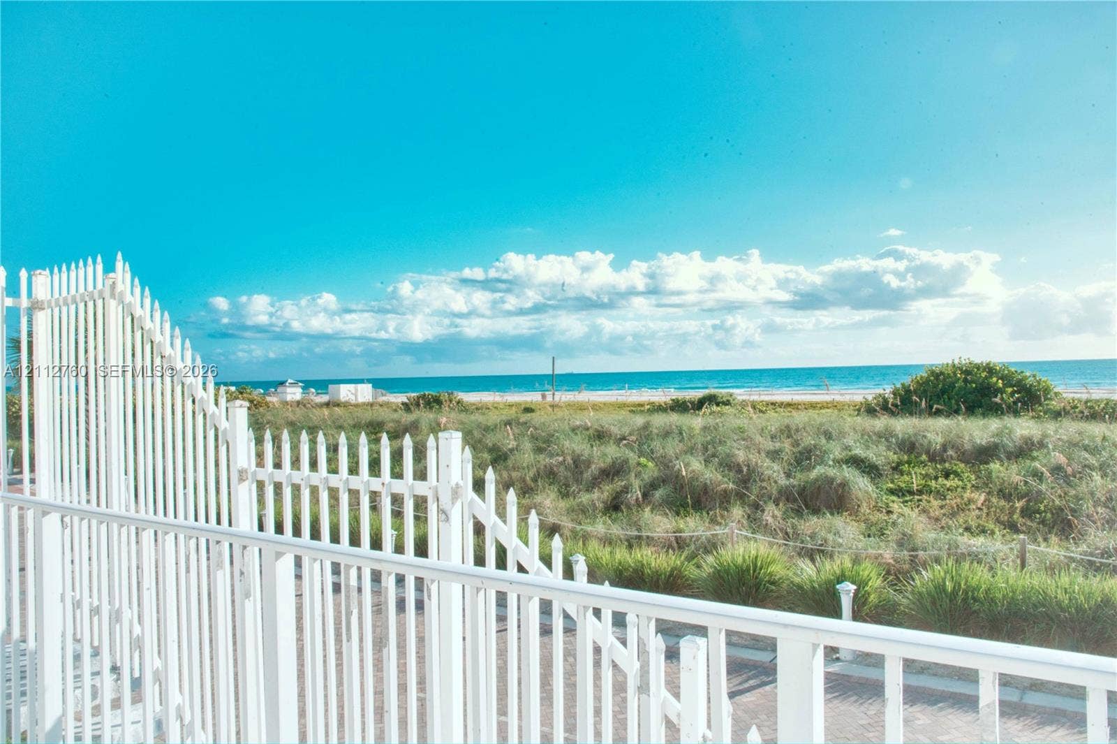 5825 Collins Avenue, #11H, Miami Beach, FL 33140 White picket fencing bordering a paved surface with coastal vegetation and ocean frontage