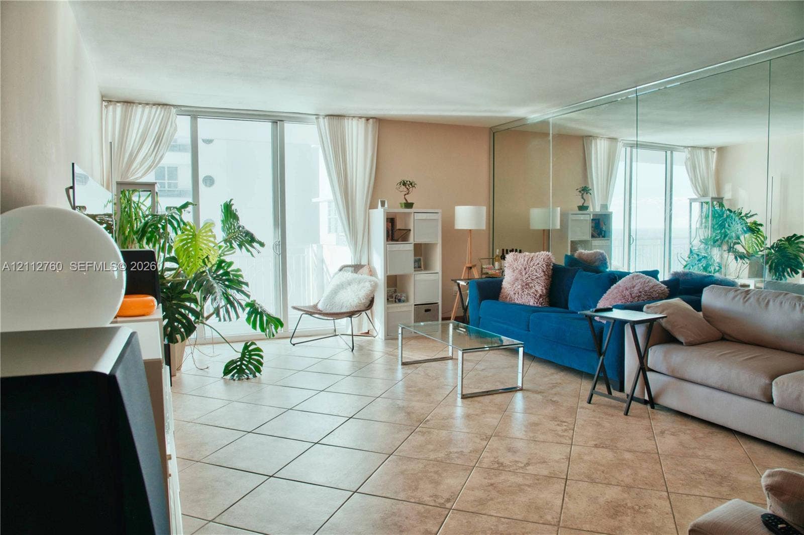 5825 Collins Avenue, #11H, Miami Beach, FL 33140 Living area featuring large-format ceramic tile flooring, floor-to-ceiling glass sliding doors, and a full-length mirrored wall