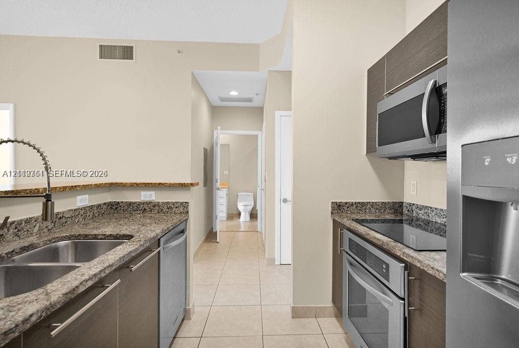 550 Okeechobee Boulevard, #224, West Palm Beach, West Palm Beach, FL 33401 Kitchen featuring dark wood-finish cabinetry, granite countertops, tile flooring, and stainless steel appliances including a built-in microwave, range, and dishwasher