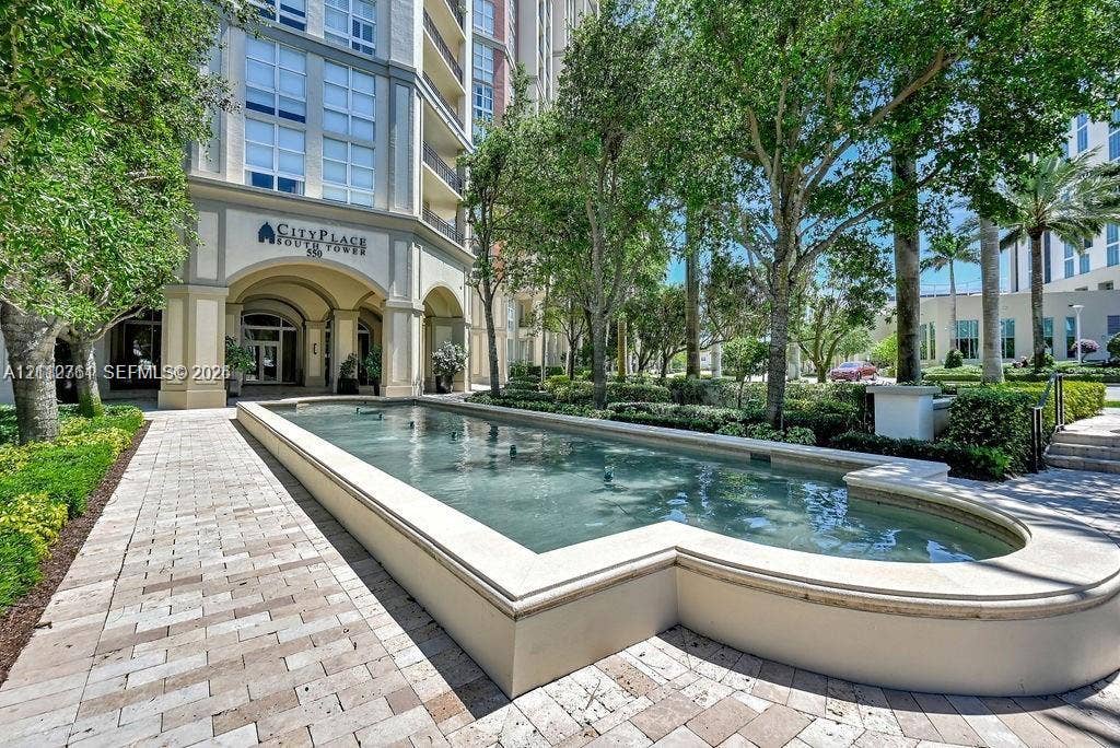 550 Okeechobee Boulevard, #224, West Palm Beach, West Palm Beach, FL 33401 Multi-story exterior featuring a stone-clad building facade, arched entryway, paved pedestrian walkway, and a formal reflecting pool surrounded by mature landscaping