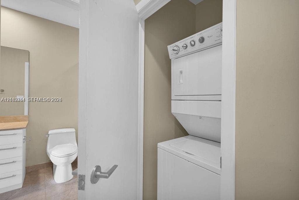 550 Okeechobee Boulevard, #224, West Palm Beach, West Palm Beach, FL 33401 Laundry closet featuring a white stacked washer and dryer unit, neutral-toned walls, a white vanity with a neutral stone-finish countertop, and a white porcelain commode