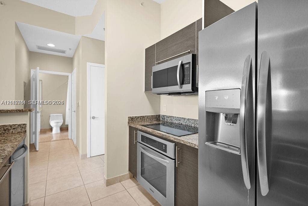 550 Okeechobee Boulevard, #224, West Palm Beach, West Palm Beach, FL 33401 Kitchen featuring dark-toned flat-panel cabinetry, stone countertops, stainless steel appliances, and tile flooring