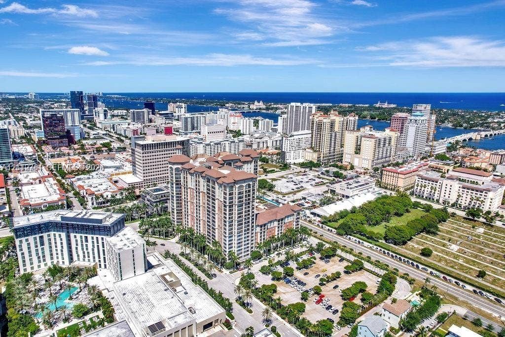 550 Okeechobee Boulevard, #224, West Palm Beach, West Palm Beach, FL 33401 Aerial perspective featuring a high-rise residential structure, urban cityscape, dense foliage, paved parking areas, and a coastal waterway backdrop
