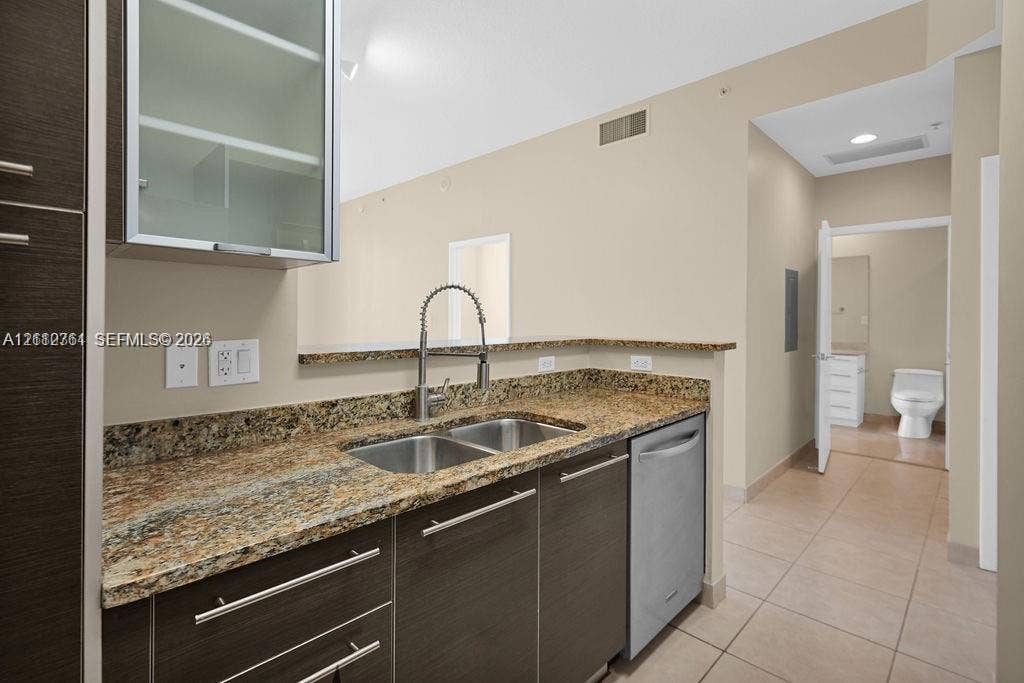 550 Okeechobee Boulevard, #224, West Palm Beach, West Palm Beach, FL 33401 Kitchen featuring dark wood-finish cabinetry, stone-surface countertops, dual-basin stainless steel sink with high-arc faucet, and stainless steel dishwasher