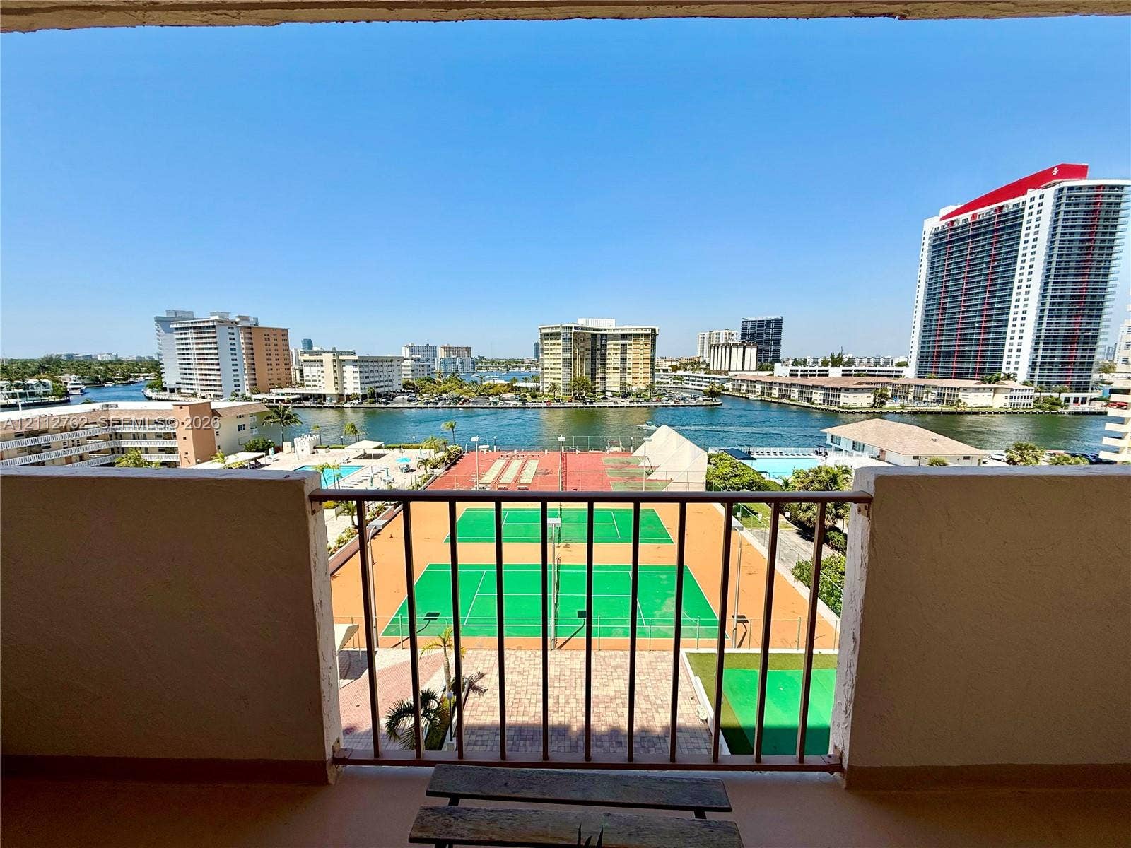 Private balcony featuring a metal railing, overlooking dual tennis courts and a waterfront canal