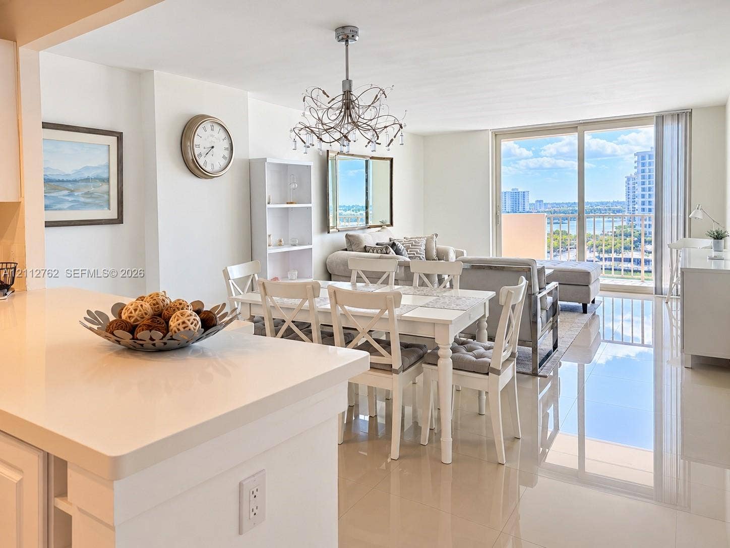 Open-concept living space featuring high-gloss tile flooring, floor-to-ceiling sliding glass doors, a decorative multi-arm chandelier, and a kitchen peninsula with solid-surface countertops
