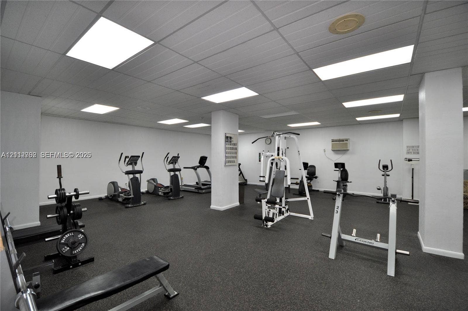 Fitness center featuring a rubberized flooring surface, drop ceiling panels, and integrated recessed lighting