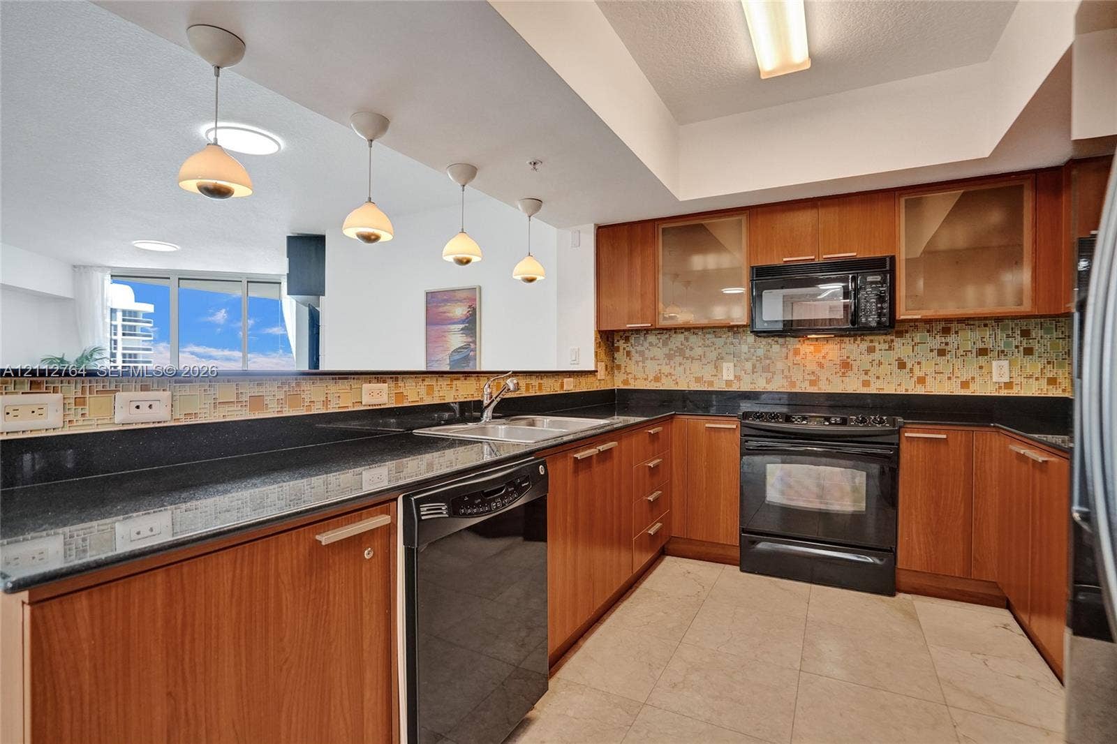Kitchen featuring natural wood-finish cabinetry, dark solid-surface countertops, multi-toned glass tile backsplash, tile flooring, and four pendant lights