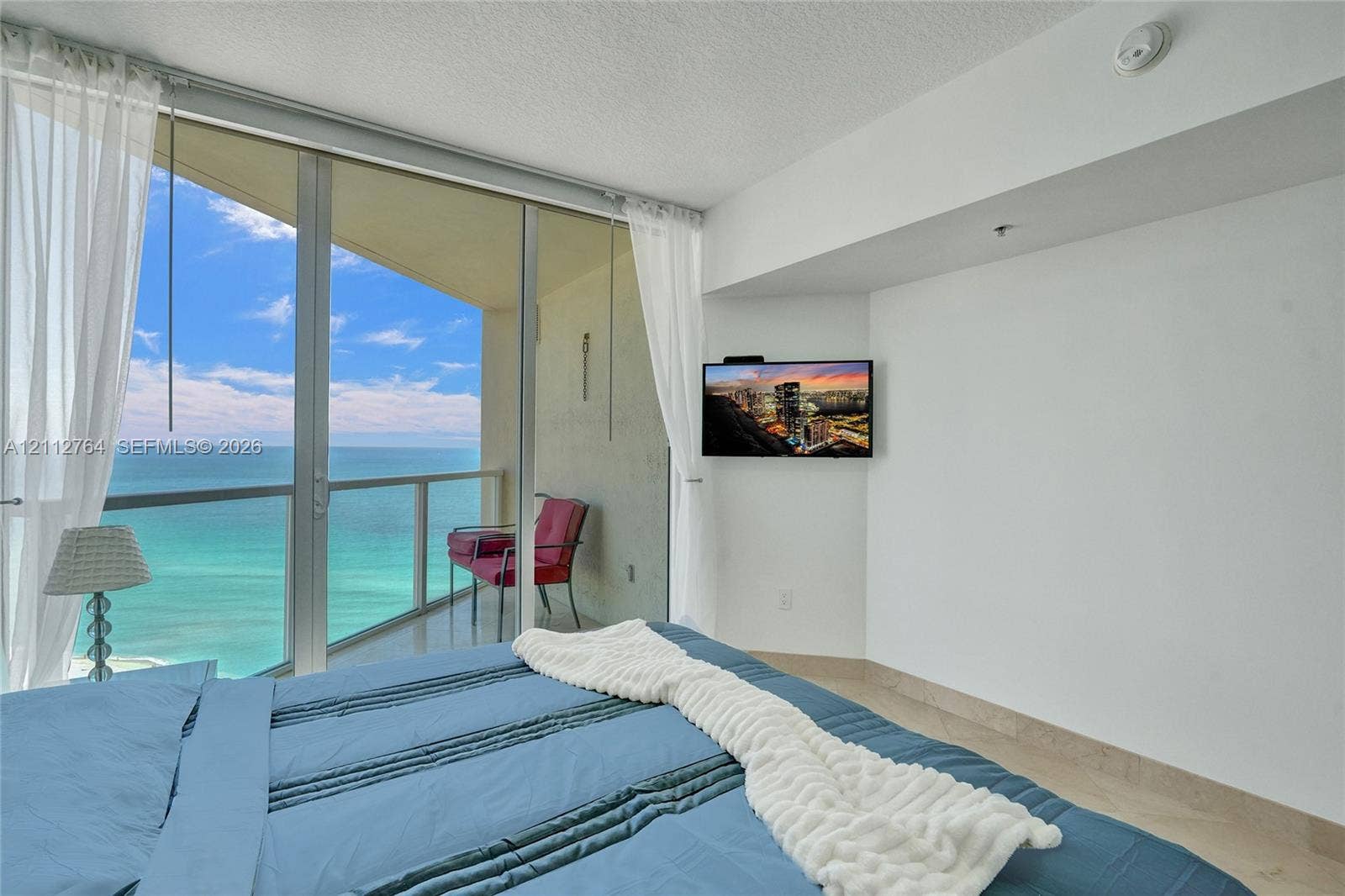 Floor-to-ceiling glass sliding doors, private balcony, glass-panel railing, and ocean horizon