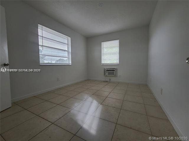 Neutral-toned tile flooring, dual windows with horizontal blinds, and a wall-mounted cooling unit