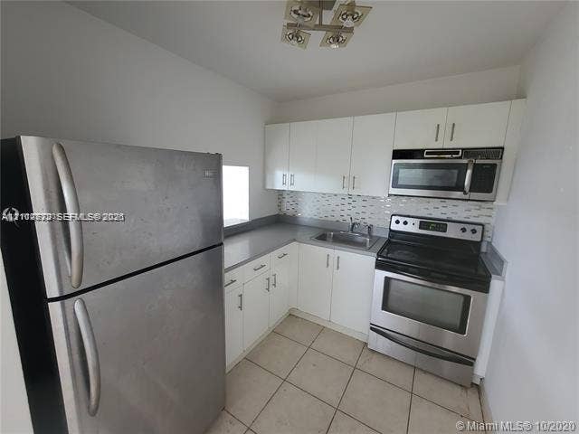 Kitchen featuring white cabinetry, stainless steel appliances, tiled backsplash, solid surface countertops, and tile flooring
