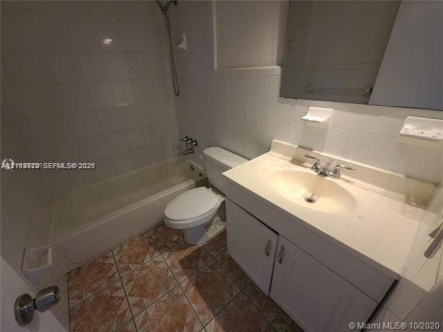 Bathroom featuring a vanity with an integrated sink, white cabinetry, a tiled bathtub surround, and patterned floor tiling