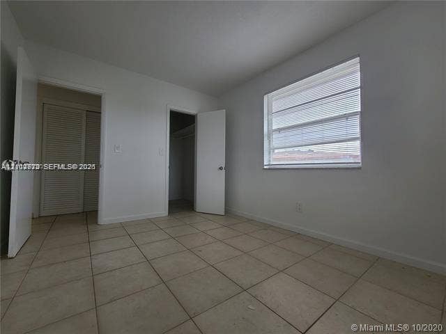 Room with tile flooring, a window featuring horizontal blinds, and a built-in closet with accordion doors
