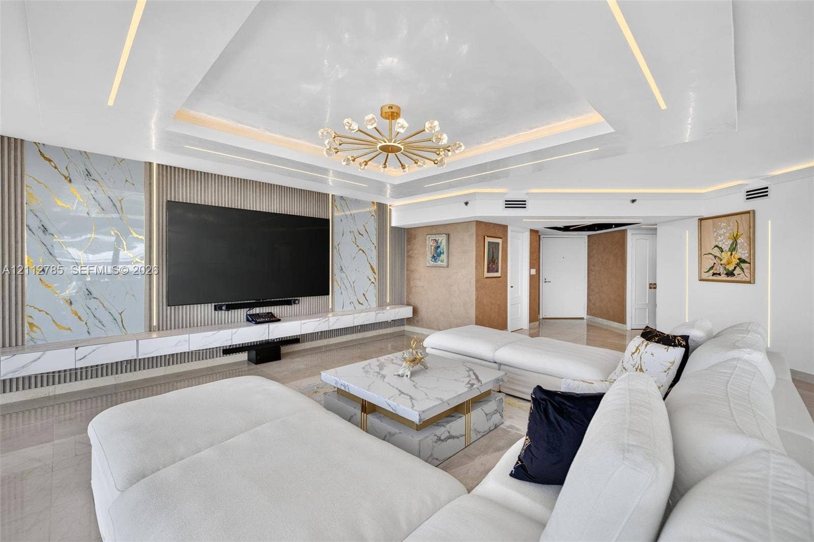 16425 Collins Avenue, #2016, Sunny Isles Beach, FL 33160 Tray ceiling featuring integrated perimeter lighting, custom stone-panel wall accents, recessed linear lighting, and a modern multi-arm chandelier