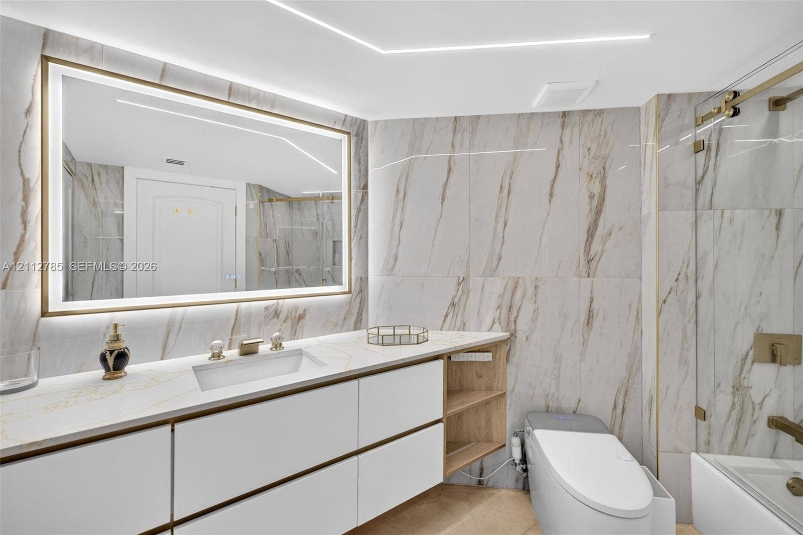 16425 Collins Avenue, #2016, Sunny Isles Beach, FL 33160 Bathroom featuring large-format stone-finish wall tile, a floating vanity with integrated cabinetry, an illuminated vanity mirror, and a glass-enclosed shower with metallic hardware