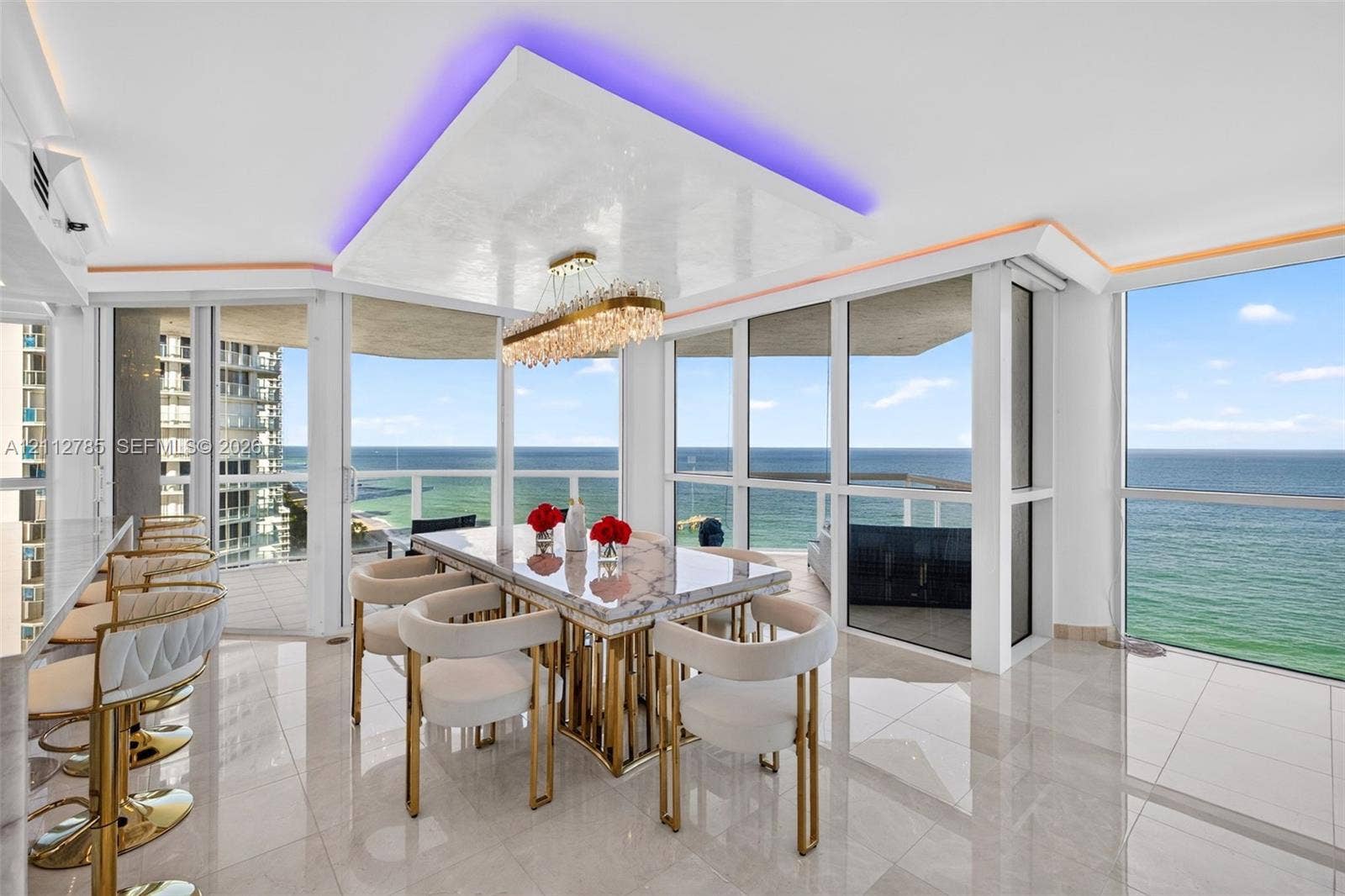 16425 Collins Avenue, #2016, Sunny Isles Beach, FL 33160 Open-concept dining area featuring floor-to-ceiling windows, polished tile flooring, a multi-tiered crystal chandelier, and a recessed ceiling cove with integrated lighting