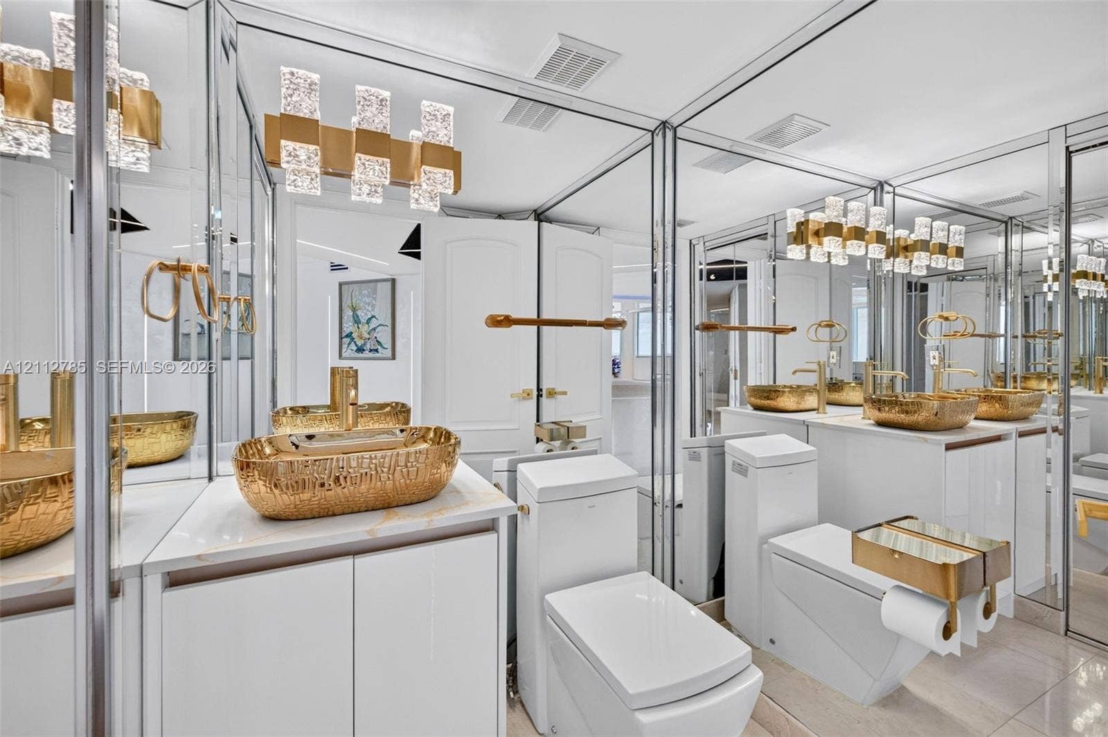 16425 Collins Avenue, #2016, Sunny Isles Beach, FL 33160 Bathroom featuring dual vanities with gold-tone hammered vessel sinks, quartz countertops, floor-to-ceiling mirrored walls, and tiered crystal-accented light fixtures