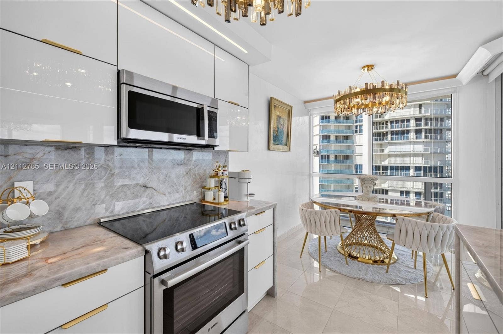 16425 Collins Avenue, #2016, Sunny Isles Beach, FL 33160 Kitchen featuring high-gloss white cabinetry, gold-tone hardware, stone-surface countertops, stone-tile backsplash, and integrated stainless steel appliances