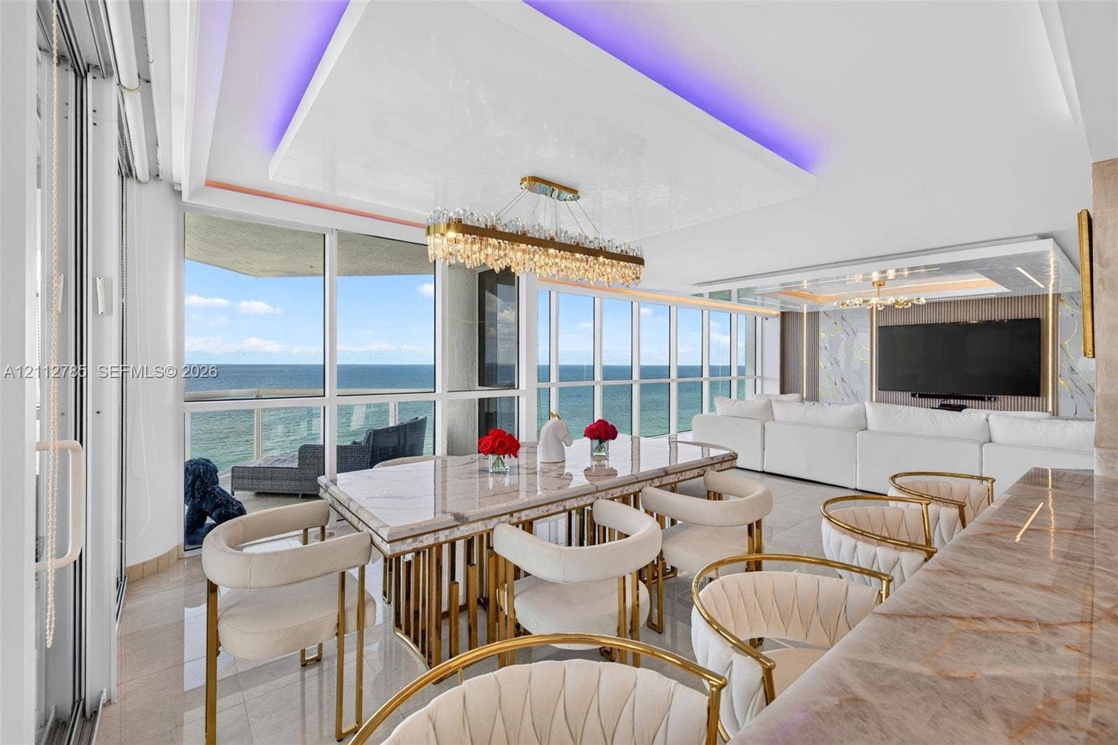 16425 Collins Avenue, #2016, Sunny Isles Beach, FL 33160 Floor-to-ceiling windows with coastal horizon, recessed tray ceiling with integrated perimeter lighting, multi-tiered crystal linear chandelier, polished stone-finish surfaces, and large-format porcelain tile flooring