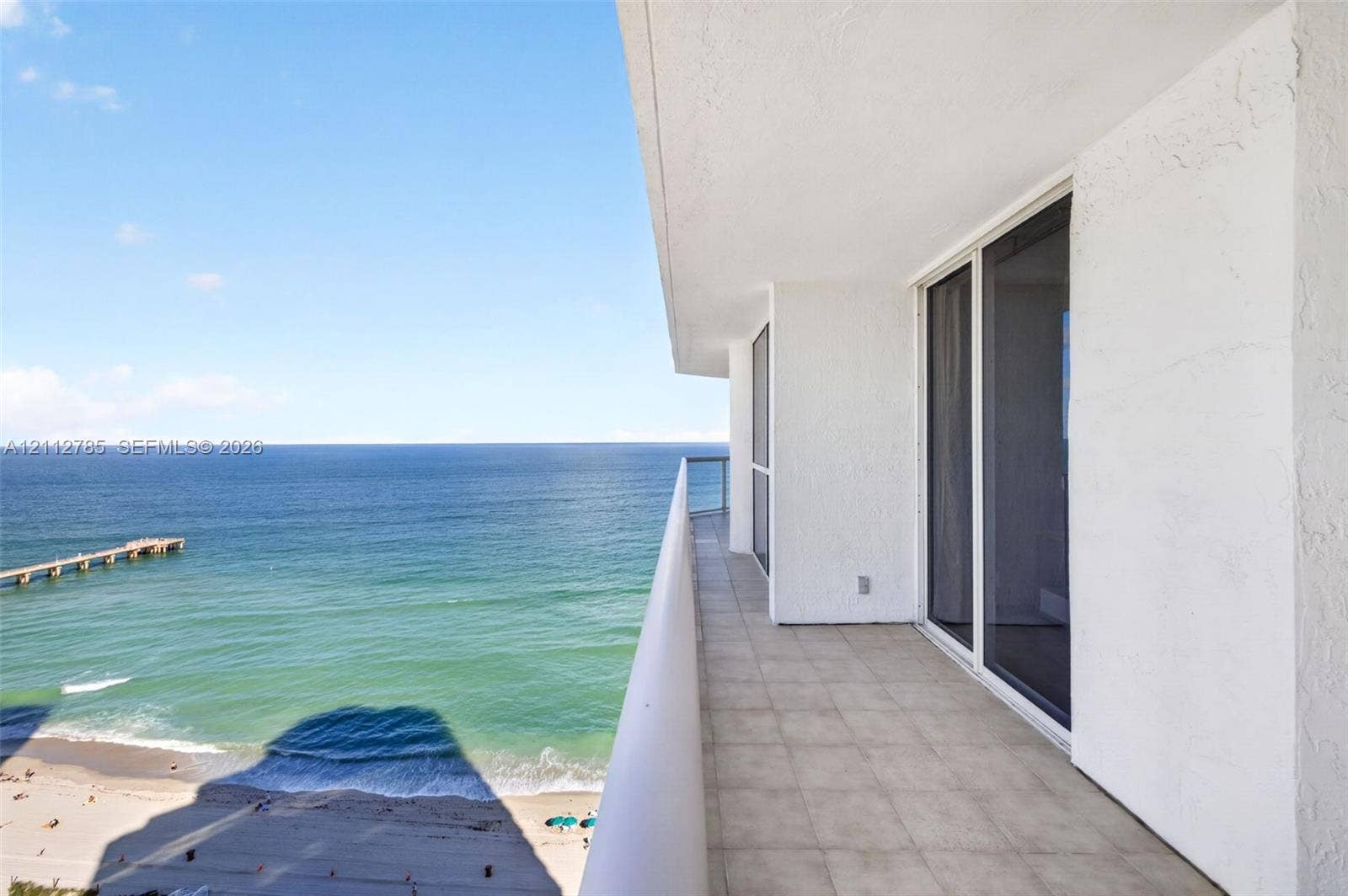 16425 Collins Avenue, #2016, Sunny Isles Beach, FL 33160 Covered balcony featuring tiled flooring, a glass panel railing, and white stucco exterior wall with sliding glass door access