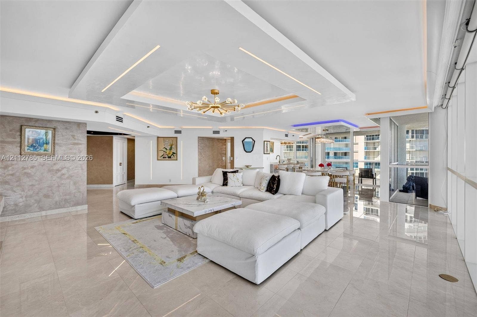 16425 Collins Avenue, #2016, Sunny Isles Beach, FL 33160 Open-concept living area featuring a custom recessed tray ceiling with integrated lighting, polished stone-finish flooring, floor-to-ceiling windows, and a textural wall finish