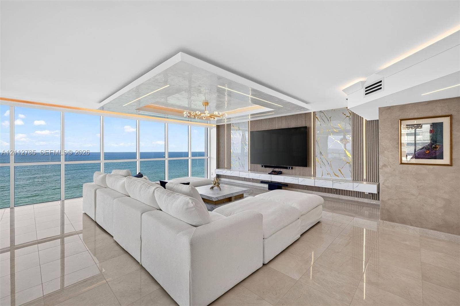 16425 Collins Avenue, #2016, Sunny Isles Beach, FL 33160 Floor-to-ceiling windows featuring ocean scenery, expansive polished tile flooring, tray ceiling with recessed lighting, and a built-in media wall with stone-finish paneling and under-cabinet illumination