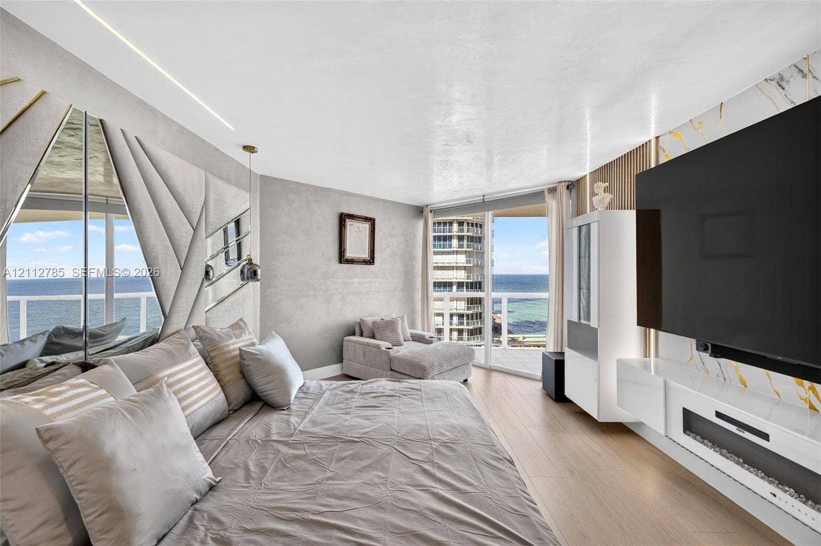 16425 Collins Avenue, #2016, Sunny Isles Beach, FL 33160 Wood-finish flooring, floor-to-ceiling windows with coastal scenery, accent wall with decorative mirror panels, wall-mounted linear fireplace, and integrated wood-slat wall paneling