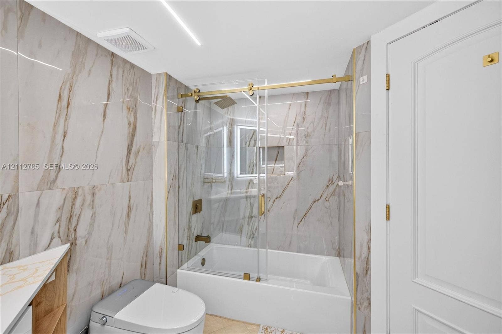 16425 Collins Avenue, #2016, Sunny Isles Beach, FL 33160 Full-height wall tiling with a vein-patterned finish, glass-enclosed shower with gold-toned hardware, built-in recessed wall niche, and modern white cabinetry