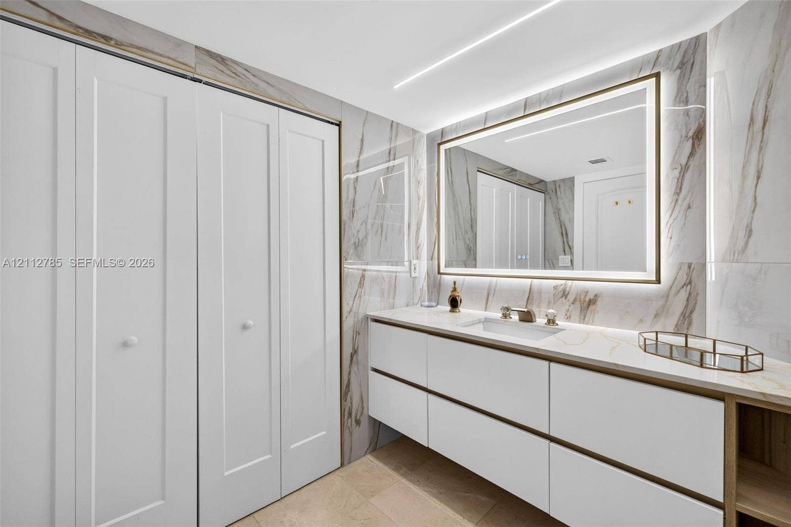 16425 Collins Avenue, #2016, Sunny Isles Beach, FL 33160 Floating vanity featuring flat-panel drawers, light-toned stone-finish countertop, integrated under-mount sink, LED-backlit mirror, and floor-to-ceiling porcelain tile wall cladding