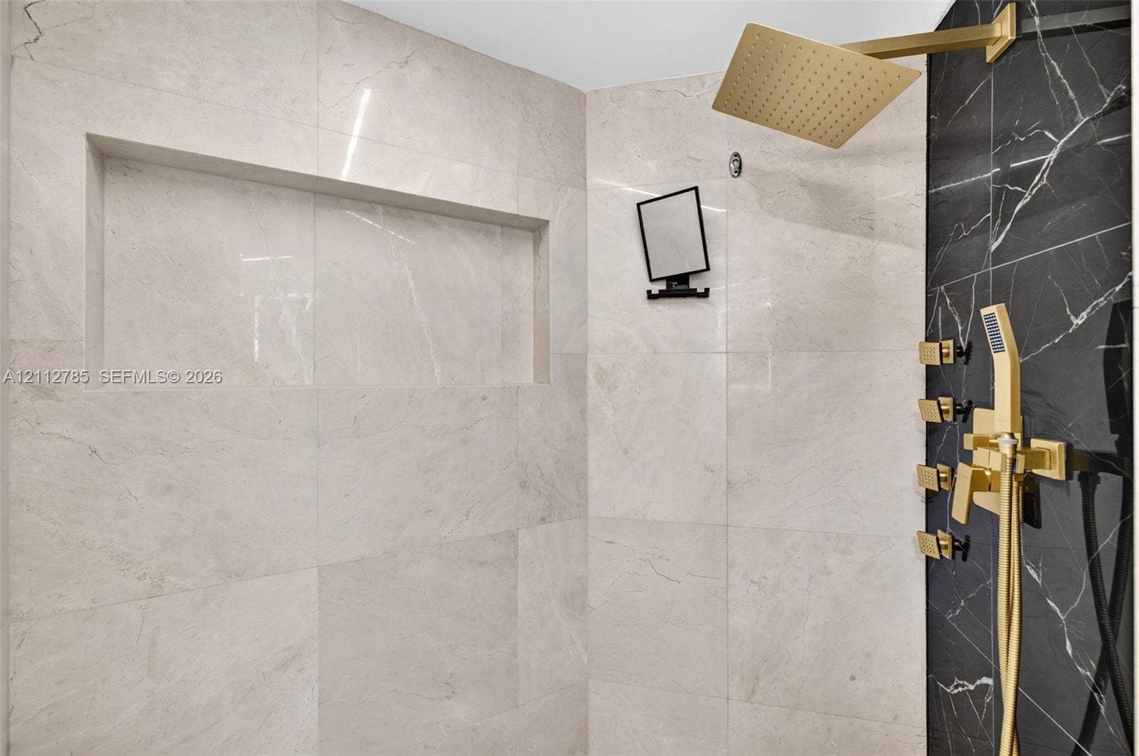 16425 Collins Avenue, #2016, Sunny Isles Beach, FL 33160 Walk-in shower featuring large-format light-tone tile, a contrasting black tile accent wall, brass finish rainfall shower head, integrated wall niche, and matching brass multi-function hand-held sprayer