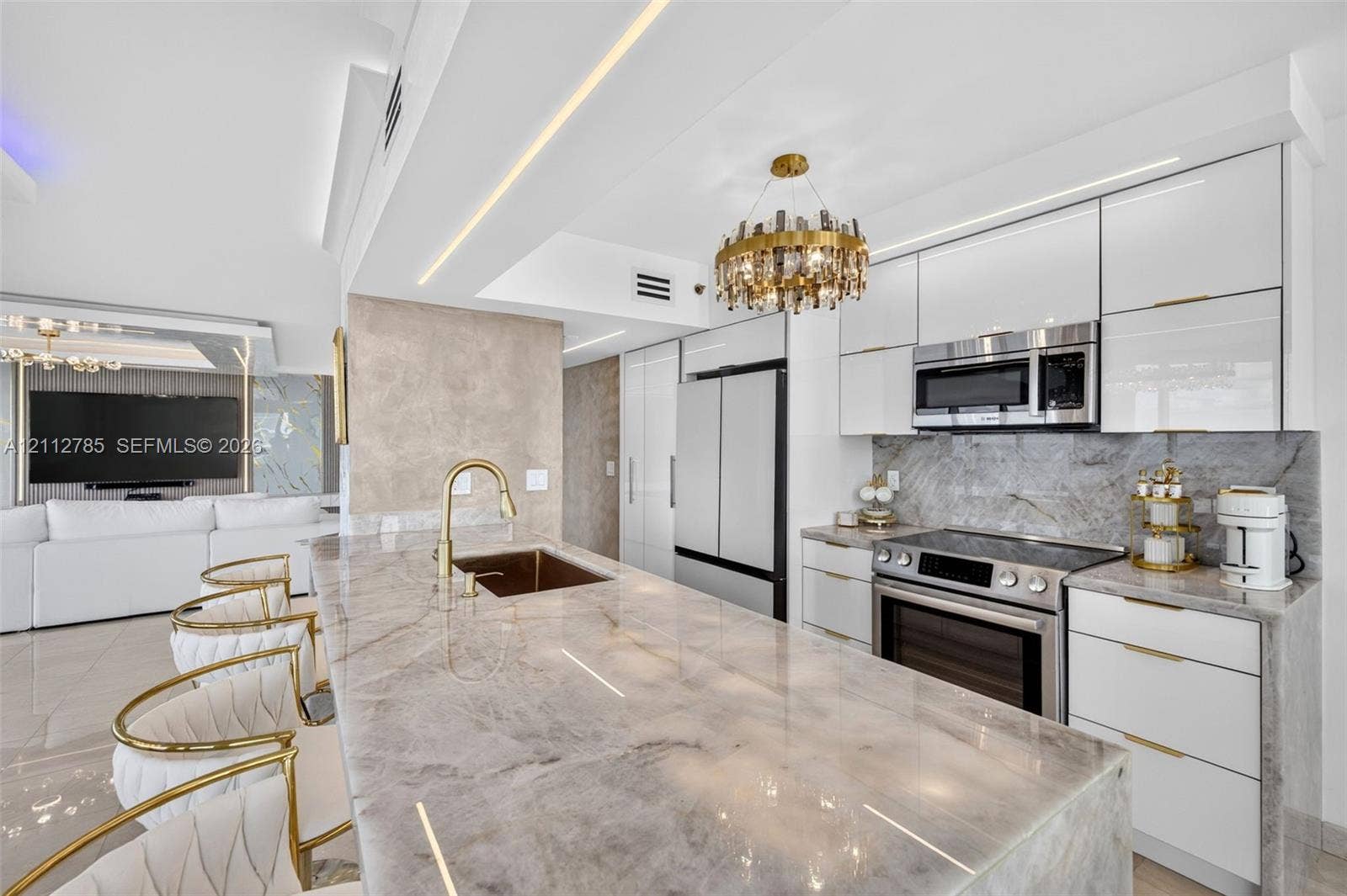 16425 Collins Avenue, #2016, Sunny Isles Beach, FL 33160 Kitchen featuring high-gloss cabinetry, stone-surface countertops, an integrated island sink with a gold-tone faucet, built-in stainless steel appliances, and a decorative circular chandelier