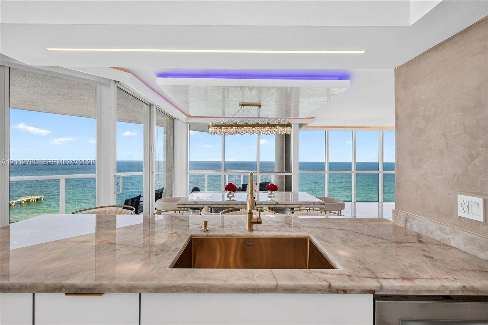 16425 Collins Avenue, #2016, Sunny Isles Beach, FL 33160 Kitchen featuring a polished stone countertop, undermount metallic basin, brushed gold-tone faucet, expansive floor-to-ceiling glass windows, and a coffered ceiling with integrated accent lighting