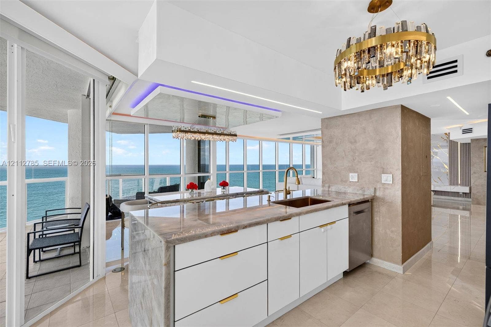 16425 Collins Avenue, #2016, Sunny Isles Beach, FL 33160 Kitchen island featuring a stone waterfall countertop, integrated stainless steel sink, gold-tone hardware, white cabinetry, and polished tile flooring