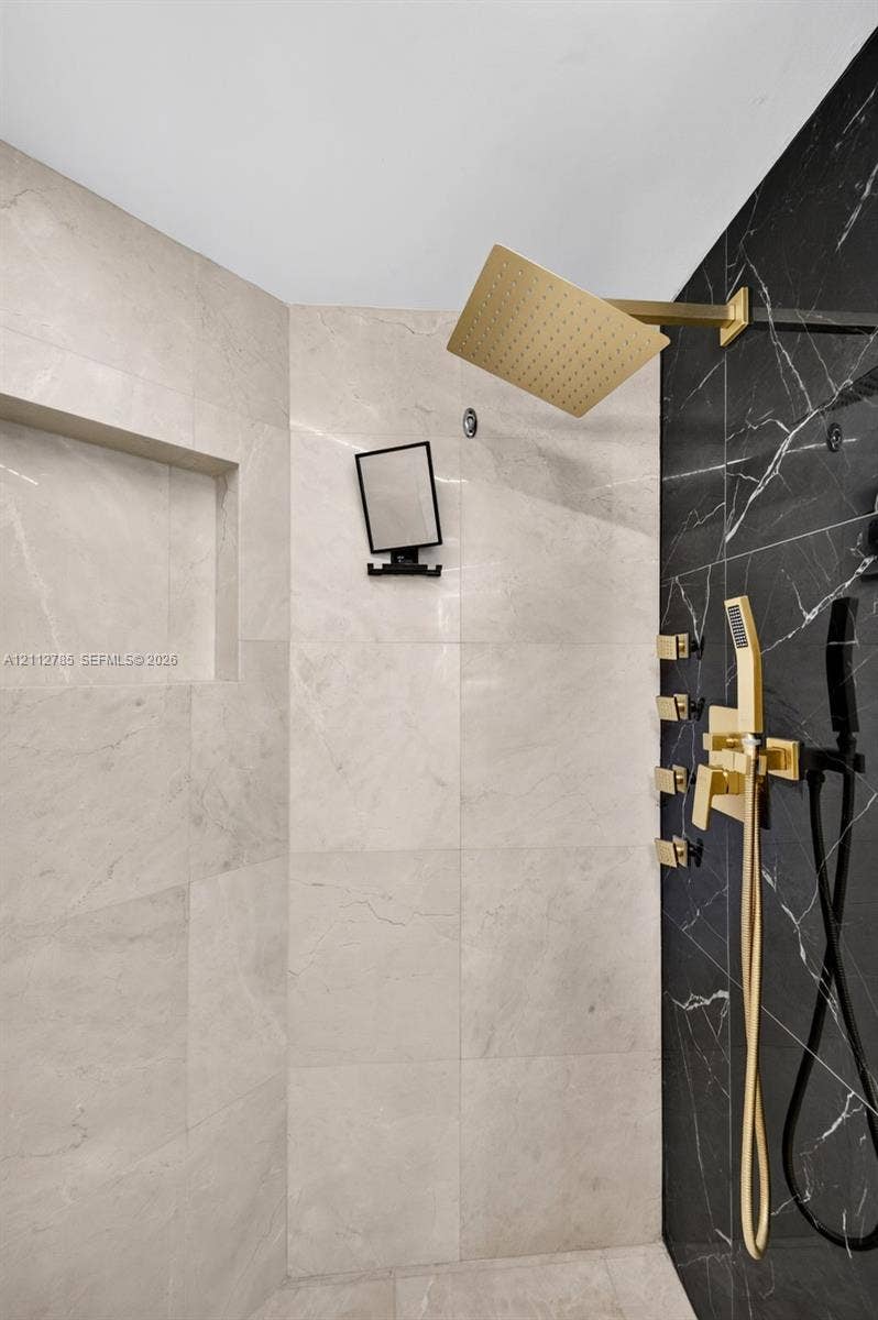 16425 Collins Avenue, #2016, Sunny Isles Beach, FL 33160 Walk-in shower featuring large-format light-toned tile, contrasting black tile accent wall, gold-finish rainfall showerhead, multi-body spray system, and integrated recessed shelving
