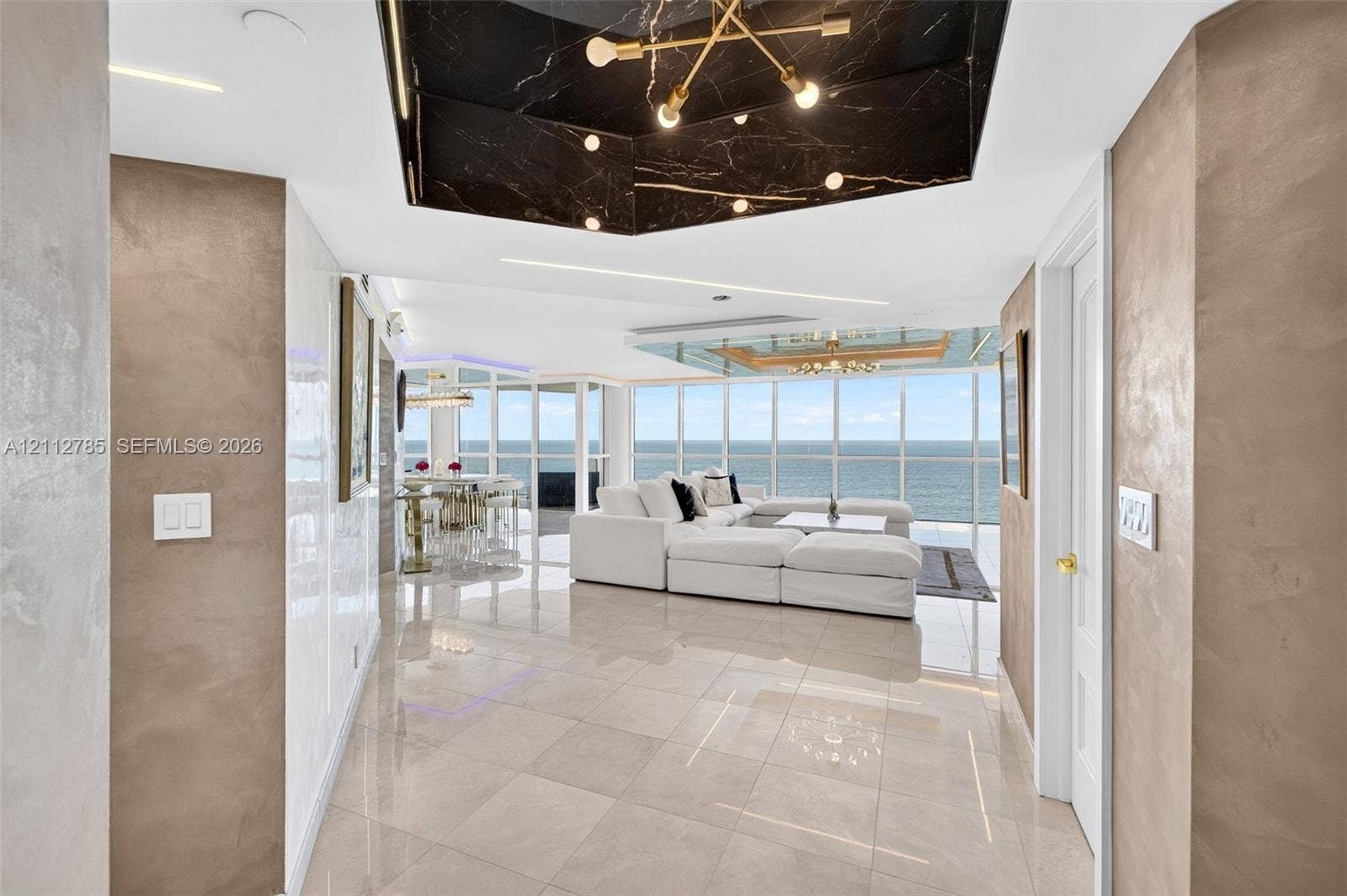 16425 Collins Avenue, #2016, Sunny Isles Beach, FL 33160 Floor-to-ceiling windows, polished tile flooring, metallic wall finishes, recessed tray ceiling with dark stone cladding, and built-in linear lighting