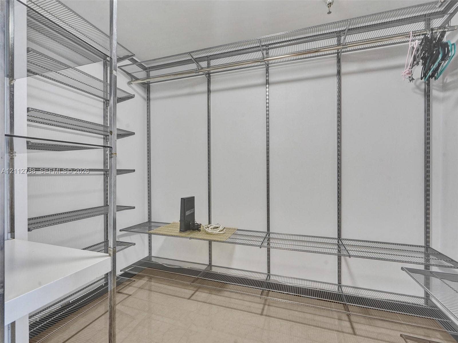 Walk-in storage space featuring adjustable metal wire shelving, integrated hanging rods, and polished tile flooring