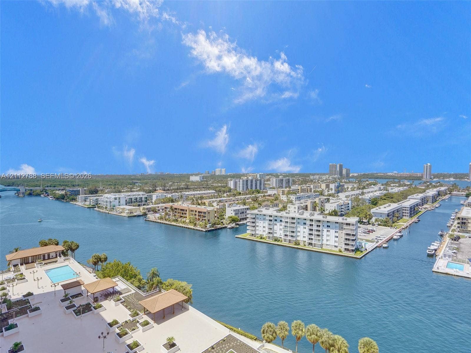 Elevated coastal perspective featuring expansive waterway exposure, a paved outdoor terrace, and a rectangular swimming pool with integrated sun deck