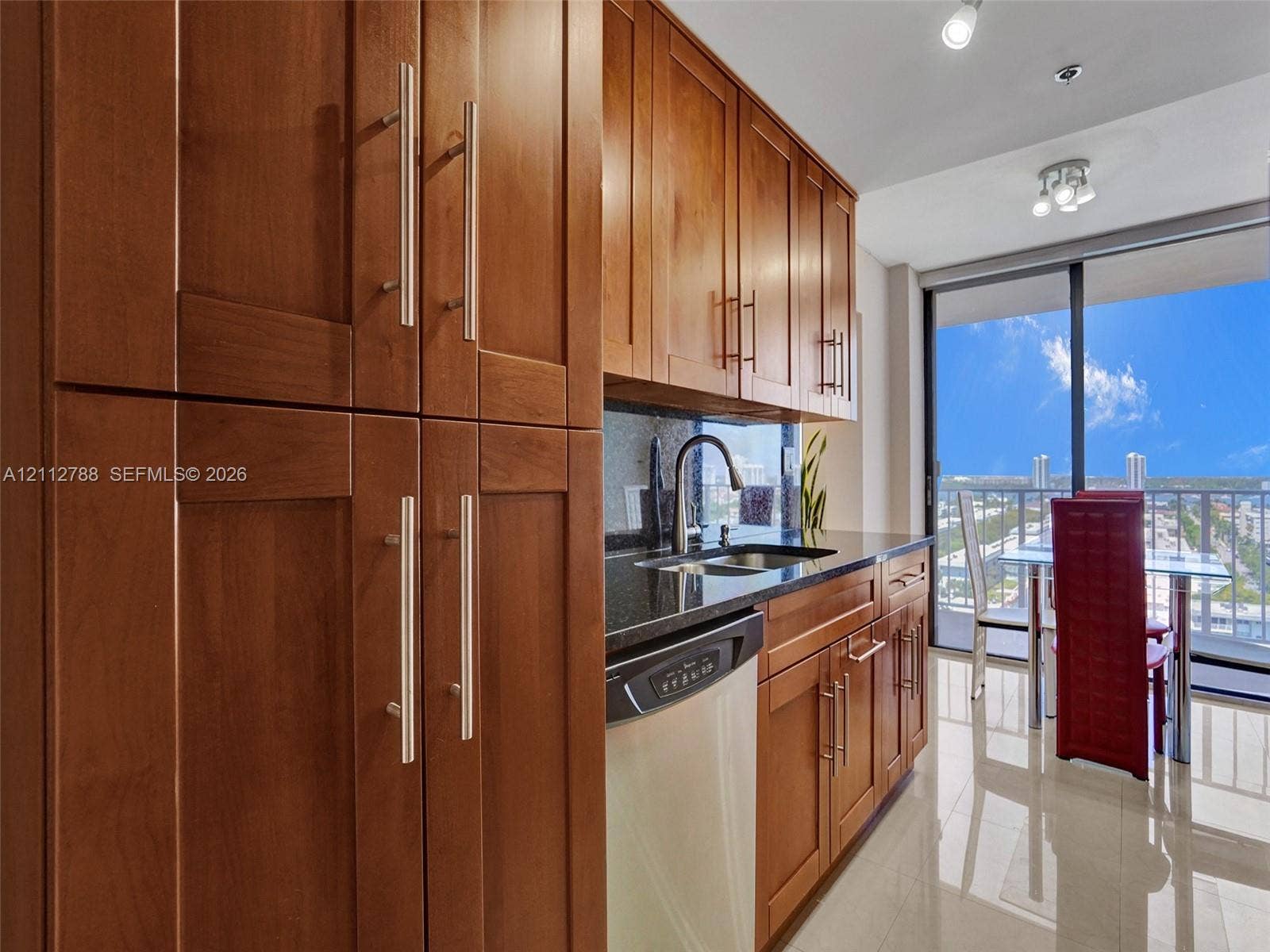 Kitchen featuring warm-toned wood cabinetry, stone countertops, stainless steel hardware, tile flooring, and floor-to-ceiling glass paneling