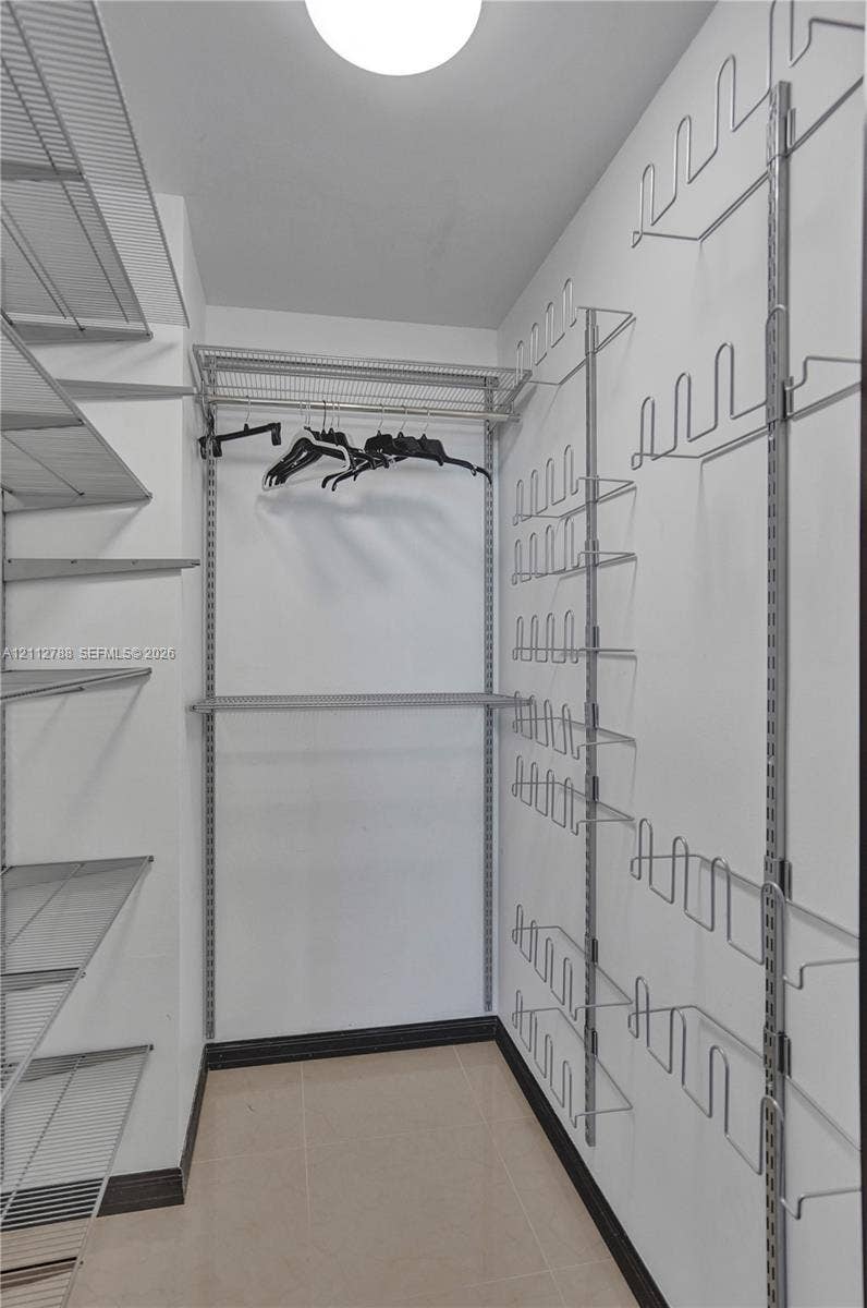 Walk-in storage space featuring adjustable metal wire shelving, dedicated rack organization for footwear, ceiling-mounted lighting, and tile flooring