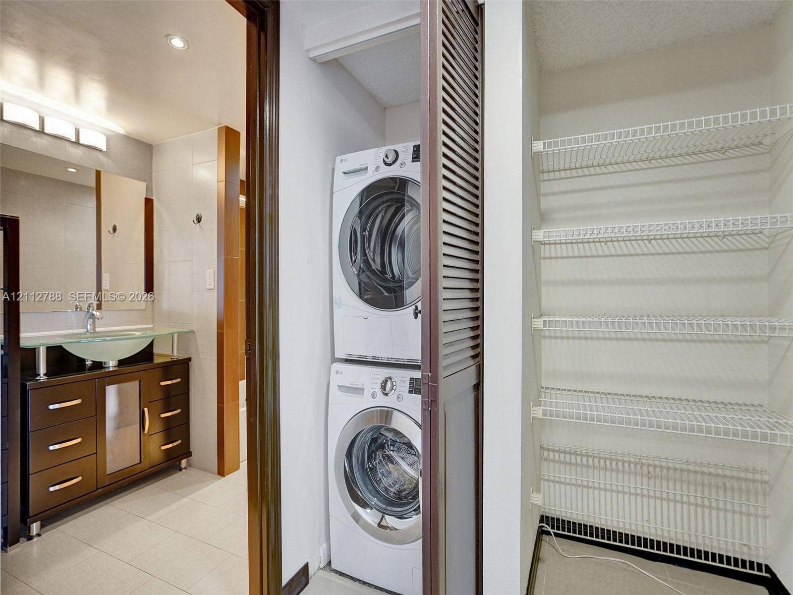 Bathroom featuring a dark wood finish vanity with a frosted glass sink basin and integrated storage, laundry closet with stacked washer and dryer, and built-in wire shelving