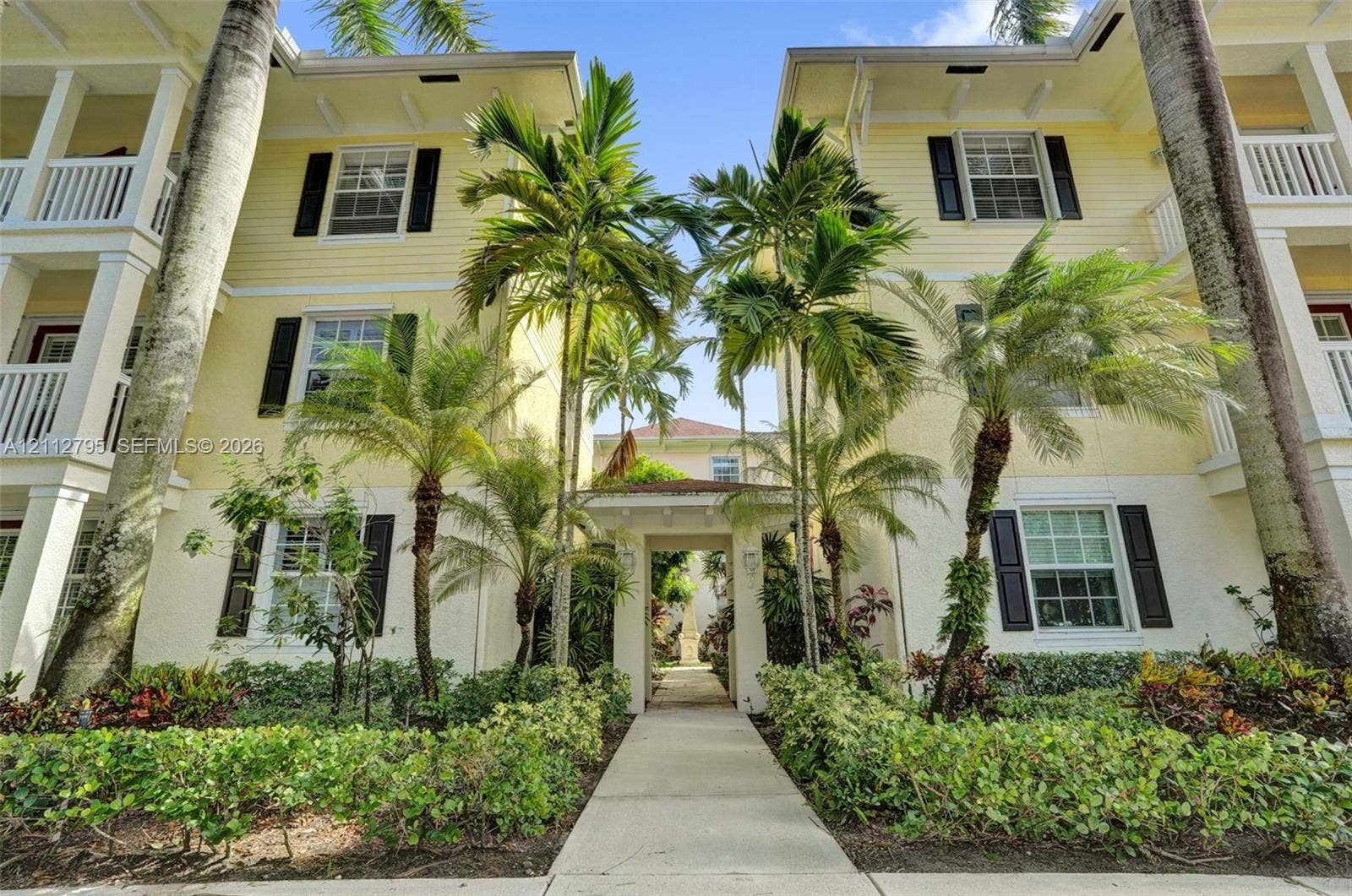 275 Murcia Drive, #205, Jupiter, FL 33458 Multi-story exterior featuring light-colored horizontal siding, dark decorative shutters, covered balconies with white railing, and mature palm landscaping