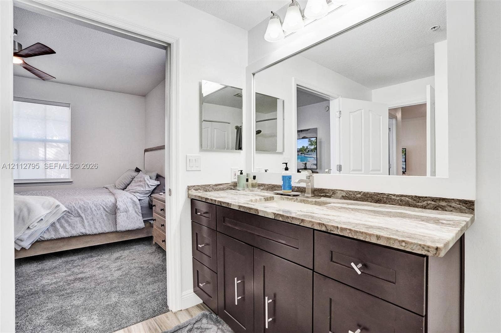 275 Murcia Drive, #205, Jupiter, FL 33458 Bathroom vanity featuring dark-toned cabinetry, a stone-patterned countertop, an integrated sink with a metal faucet, a large wall-mounted mirror, and triple-bulb vanity lighting
