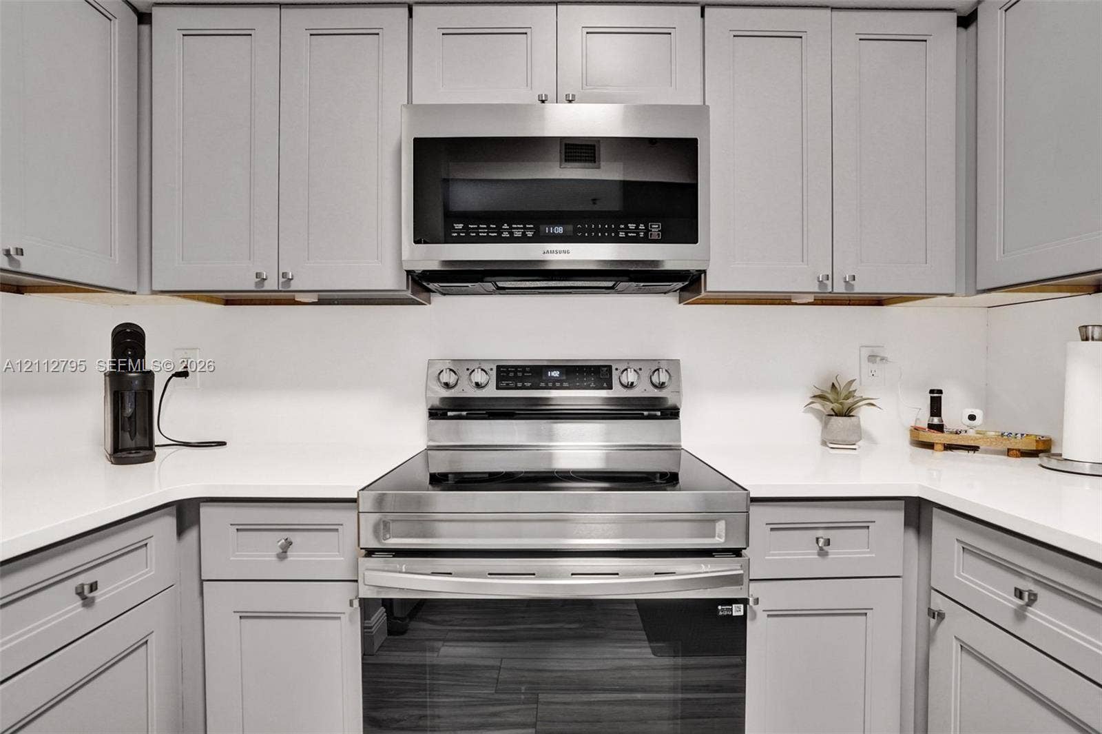 275 Murcia Drive, #205, Jupiter, FL 33458 Kitchen featuring grey shaker-style cabinetry, solid-surface countertops, and stainless steel appliances, including an over-the-range microwave and a smooth-top range
