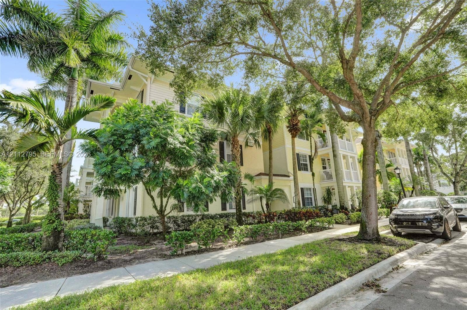 275 Murcia Drive, #205, Jupiter, FL 33458 Multi-story exterior featuring pale yellow siding, shuttered windows, covered balconies, and mature palm and oak landscaping